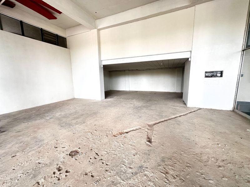 An empty, open-plan commercial space featuring high ceilings, exposed structural beams, and a raw concrete floor with visible surface wear and structural channels.