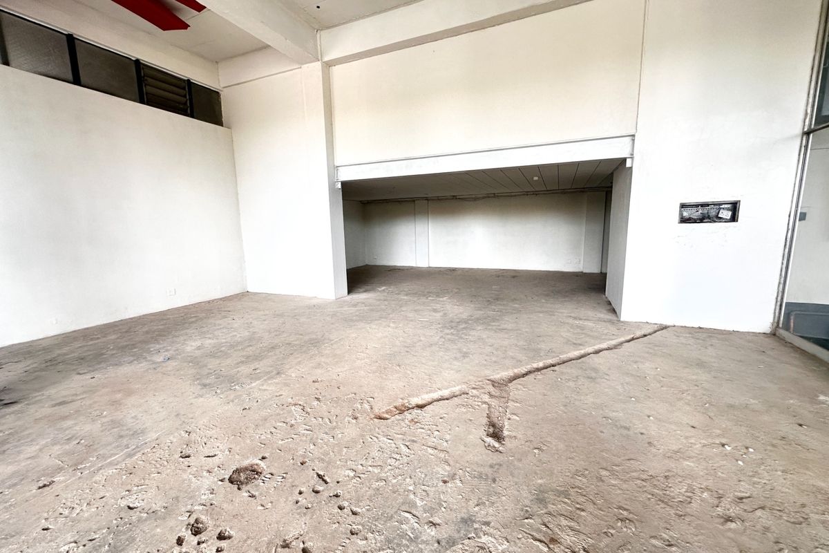 An empty, open-plan commercial space featuring high ceilings, exposed structural beams, and a raw concrete floor with visible surface wear and structural channels.
