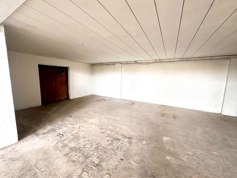An empty, unfinished utility space featuring exposed concrete flooring, a panelled ceiling, and visible electrical conduit, suitable for storage or workshop conversion.
