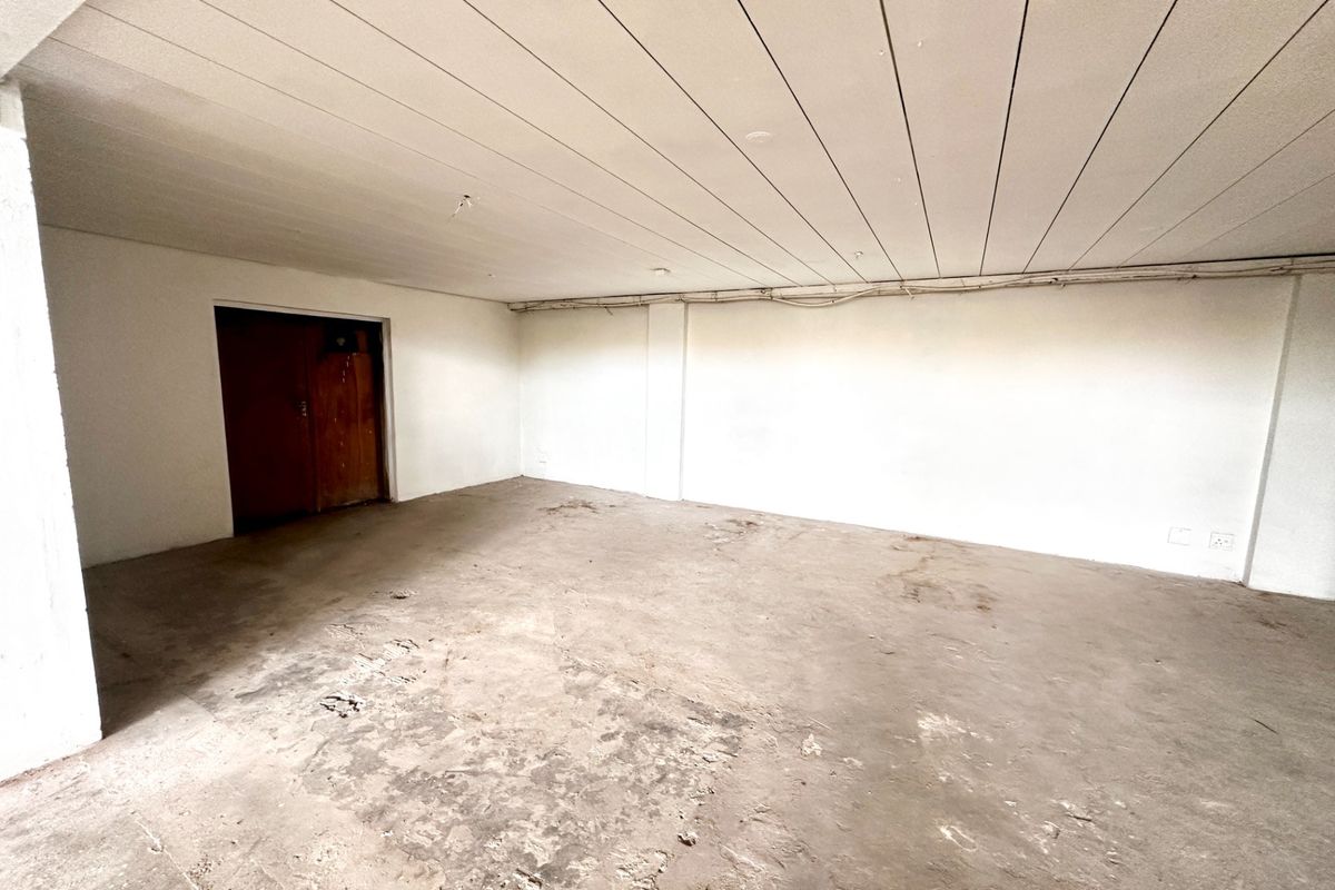 An empty, unfinished utility space featuring exposed concrete flooring, a panelled ceiling, and visible electrical conduit, suitable for storage or workshop conversion.