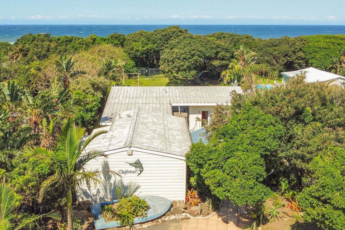 Aerial view of a coastal property featuring a metal roof, weatherboard exterior, and lush surrounding vegetation with ocean views in the background.