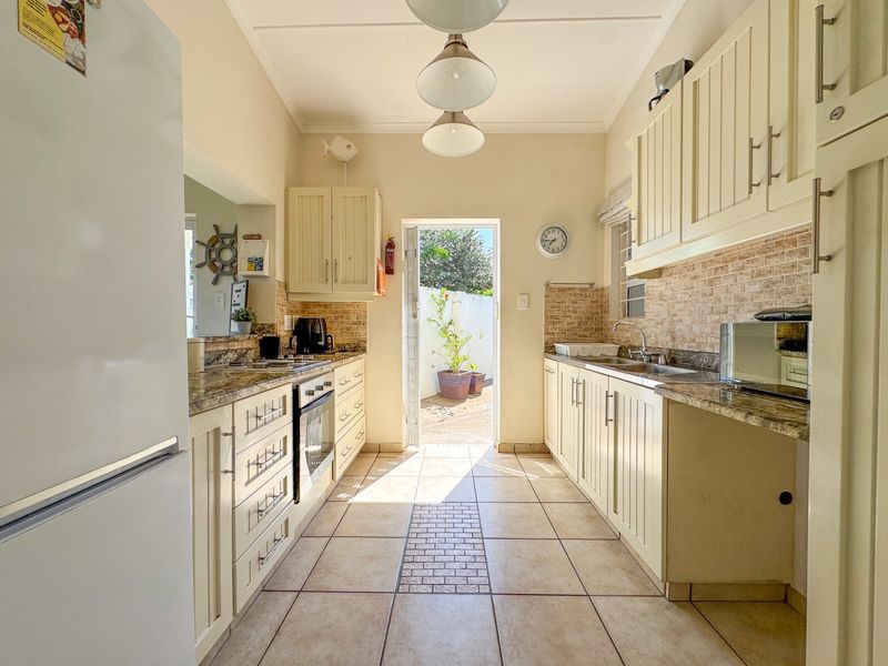 A functional galley-style kitchen featuring cream cabinetry, granite countertops, tiled backsplash, and direct access to an outdoor area.