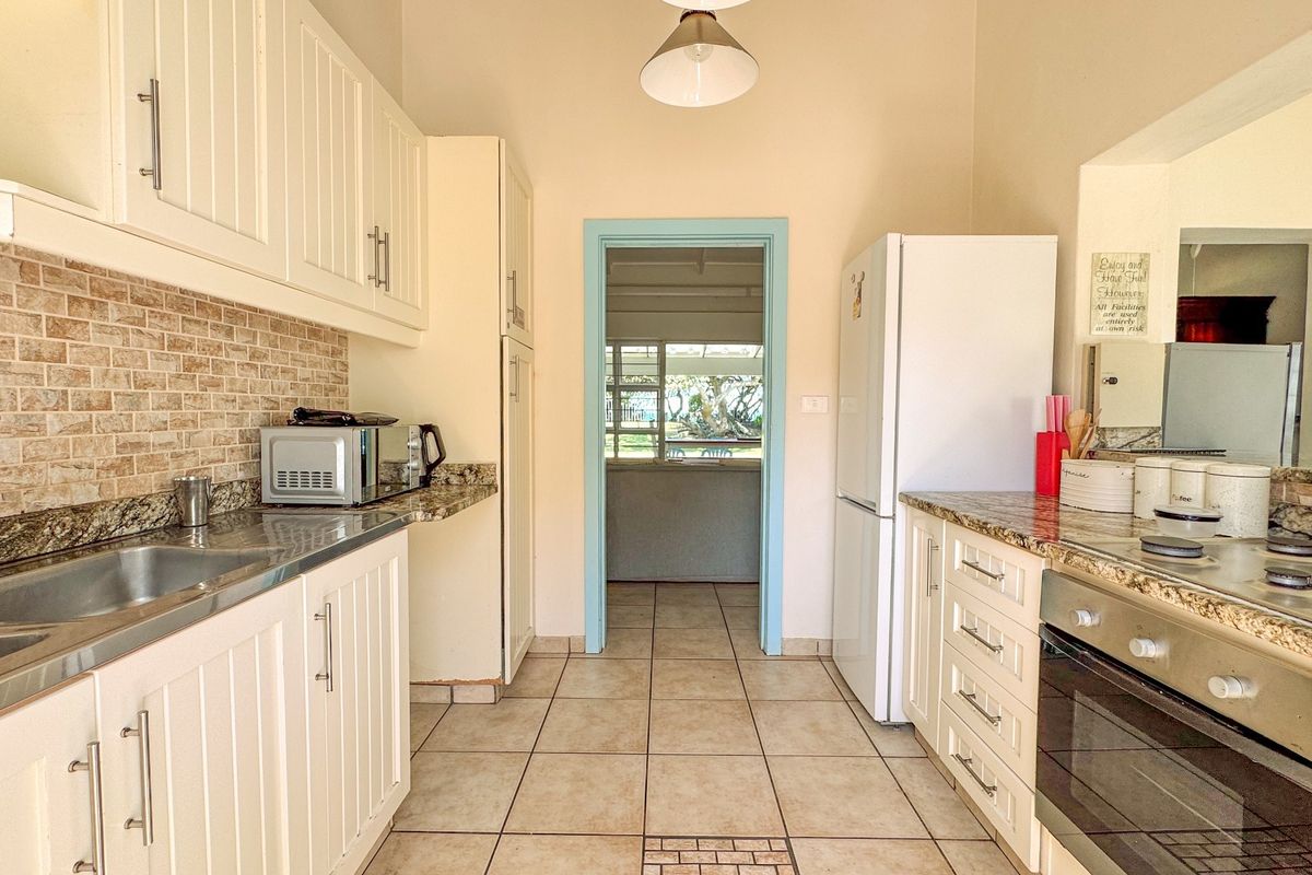 A functional kitchen featuring granite countertops, built-in cabinetry, a stainless steel sink, and a built-in oven with hob, leading to an adjacent living area.