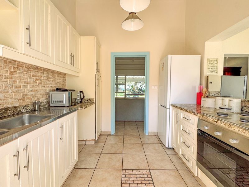 A functional kitchen featuring granite countertops, built-in cabinetry, a stainless steel sink, and a built-in oven with hob, leading to an adjacent living area.