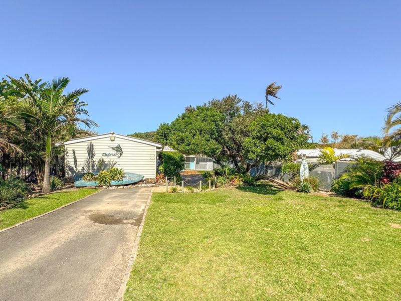 Front view of the property featuring a paved driveway, established garden, and weatherboard exterior facade.