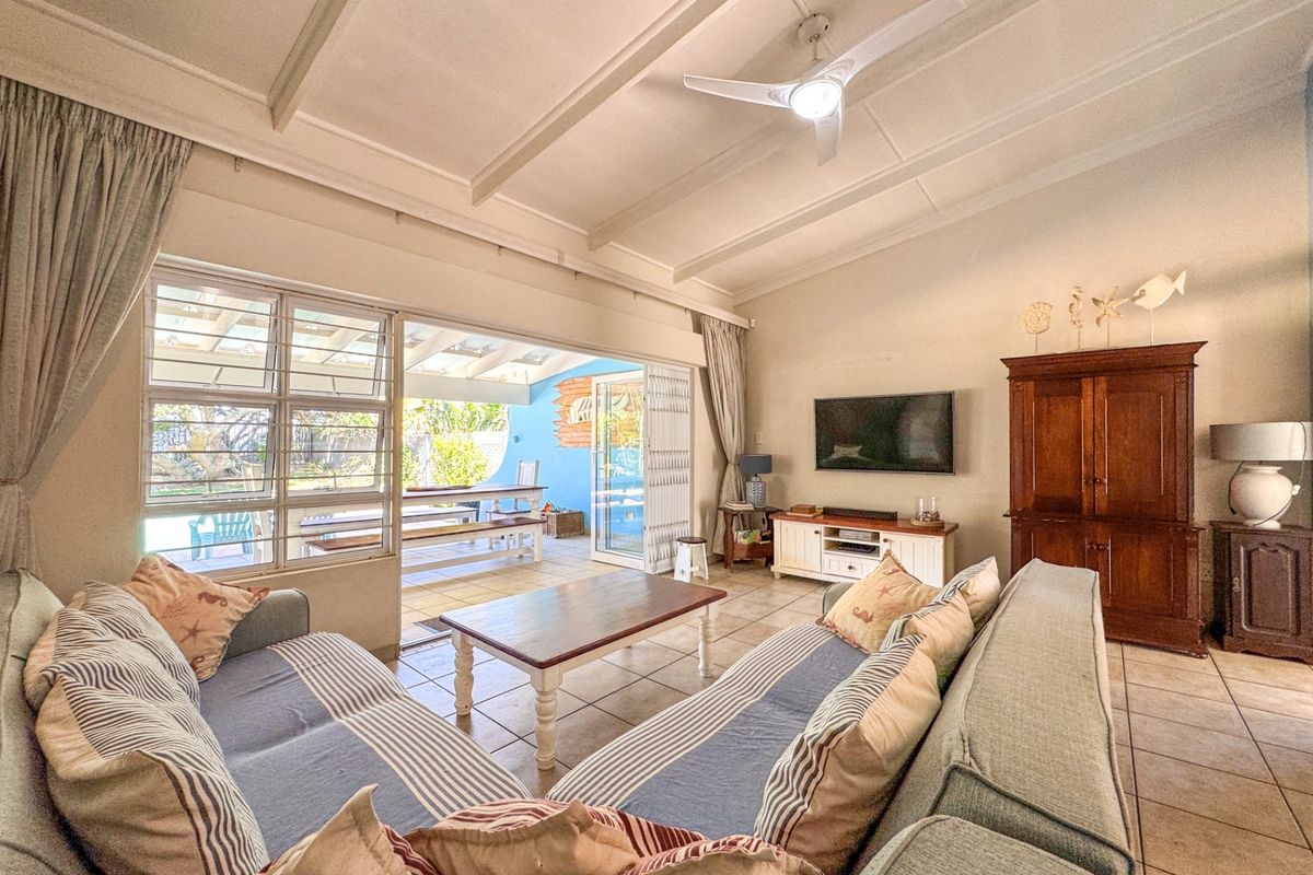 Spacious living room featuring tiled flooring, exposed beam ceiling, and large sliding doors providing seamless access to the outdoor patio area.