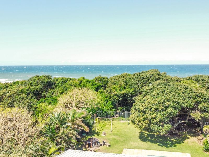 An elevated view overlooking a lush garden with mature trees and a scenic coastal ocean backdrop.
