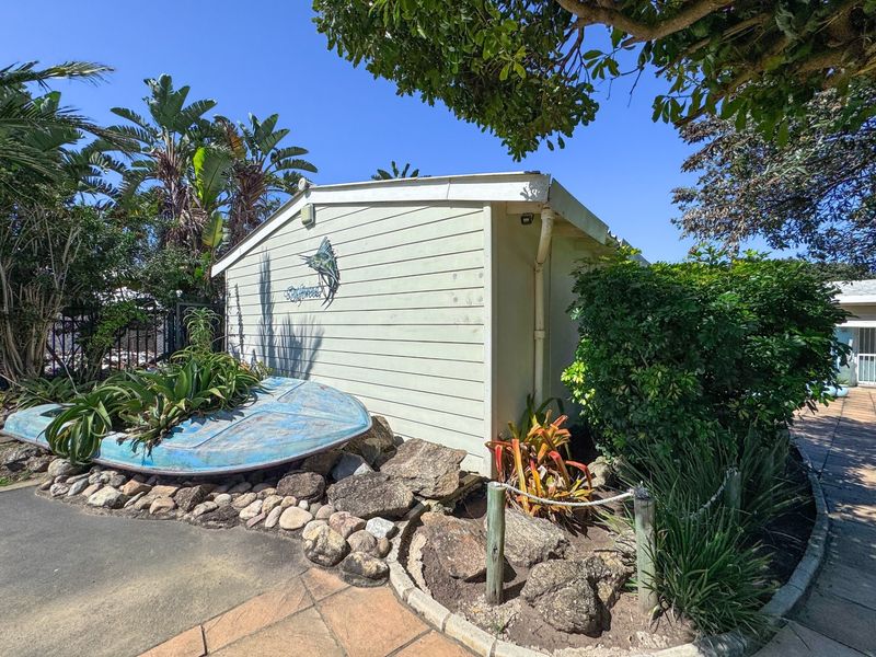 Exterior view of a weatherboard structure featuring a paved walkway and landscaped garden area.