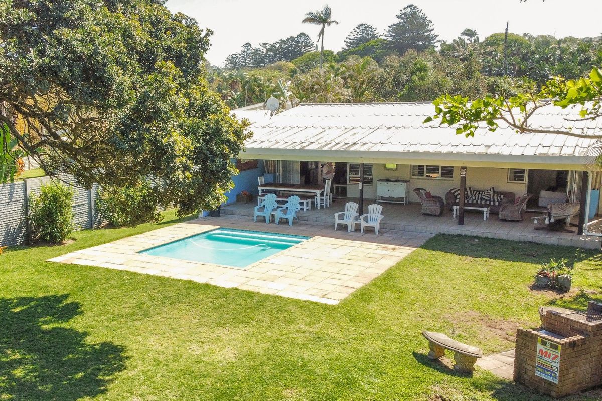 Rear exterior view featuring a swimming pool, covered patio area, and a built-in brick braai set within a spacious garden.