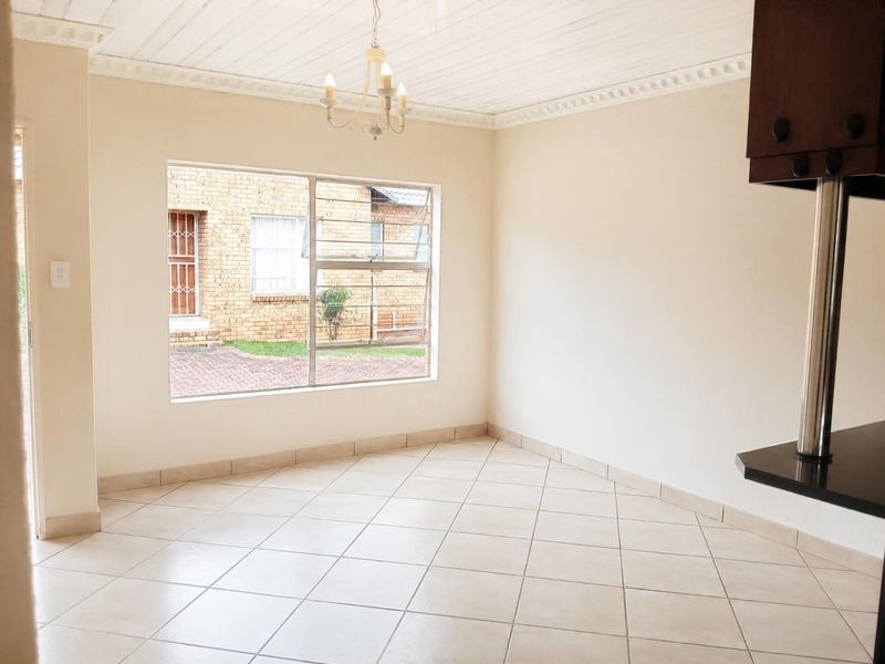 A bright, empty open-plan living area featuring neutral tiled flooring, decorative ceiling cornices, and a breakfast bar, offering a versatile space for customization.