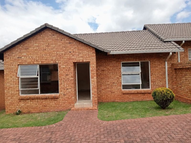 Front elevation of a face brick townhouse featuring a tiled roof, aluminium window frames, and a paved walkway leading to the entrance.