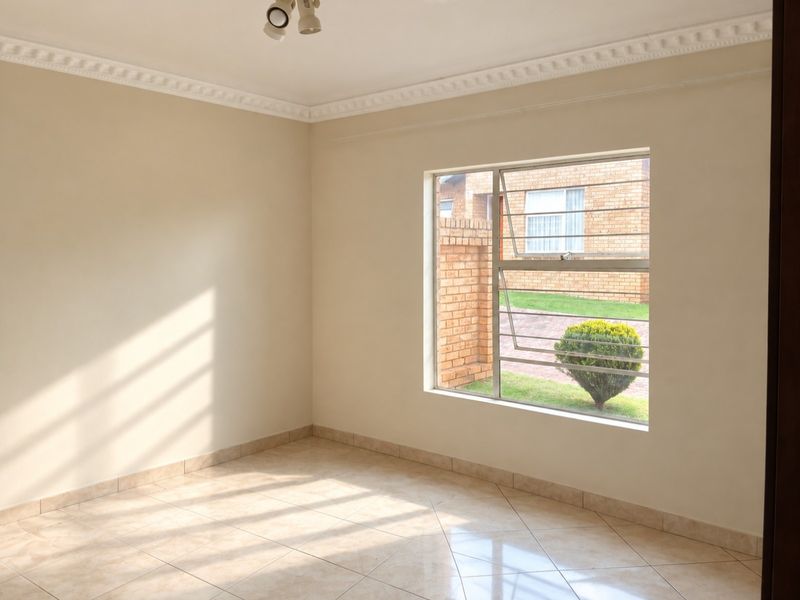 A bright, empty bedroom featuring neutral tiled flooring, decorative cornice, and a window fitted with security bars.