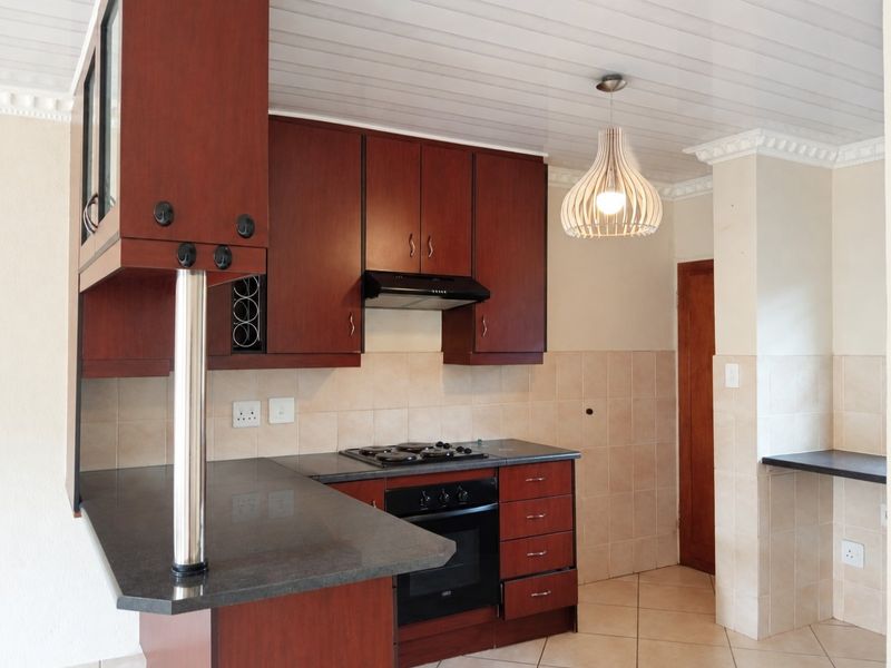 A functional kitchen featuring dark wood cabinetry, stone countertops, a built-in oven with gas hob, and tiled splashbacks in a clean, well-maintained space.