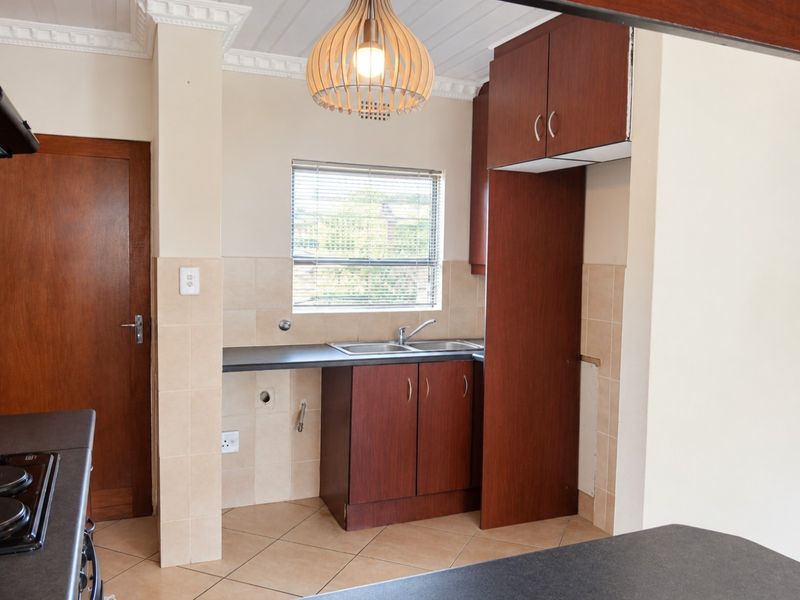 A functional kitchen featuring dark wood cabinetry, tiled backsplash, double sink, and tiled flooring, offering a clean and practical workspace.