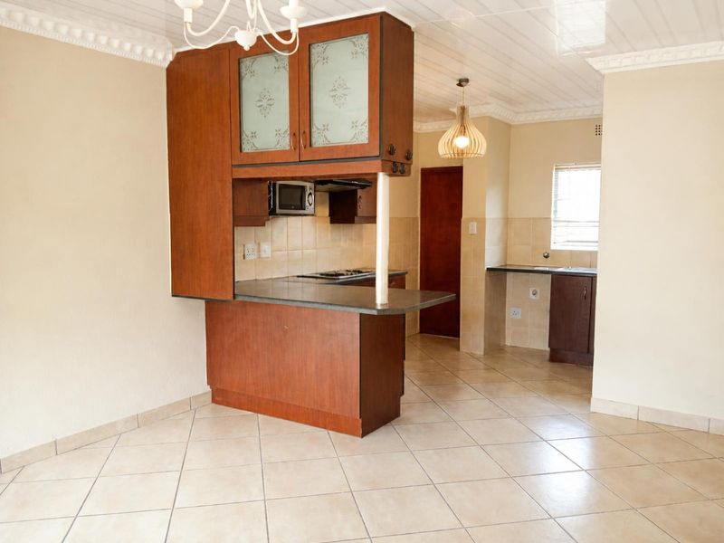 An open-plan kitchen featuring wooden cabinetry, a breakfast bar, tiled flooring, and a tiled backsplash, offering a functional layout ready for updates.