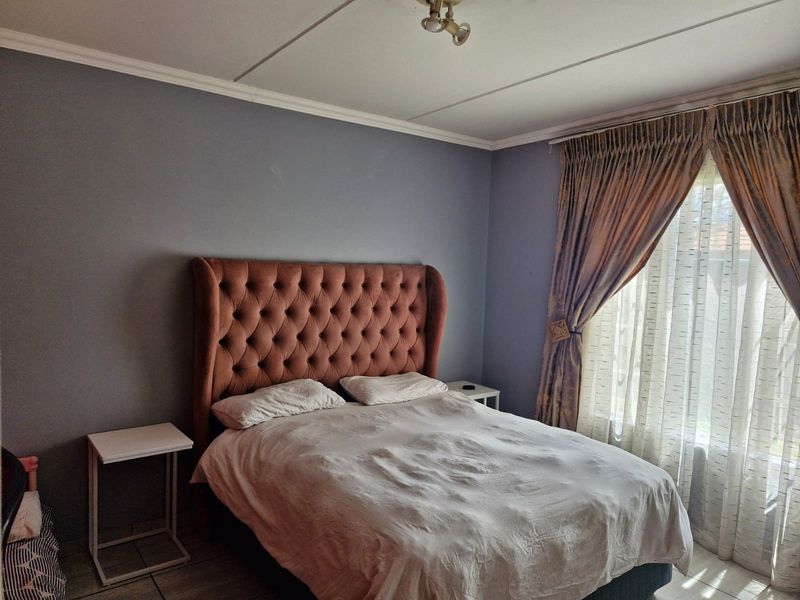 A bedroom featuring tiled flooring, neutral wall paint, and natural light provided by a window with curtain tracks.