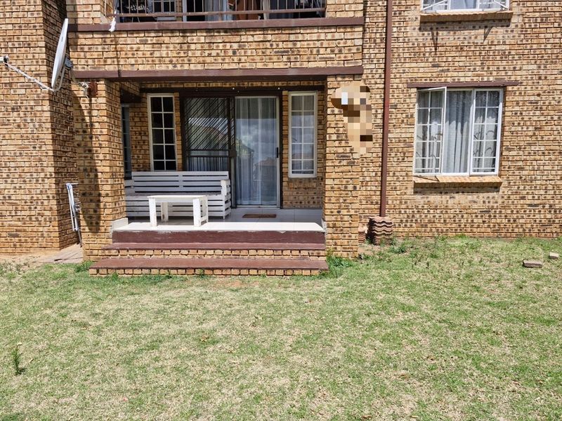 Rear view of the apartment featuring a face brick facade, a tiled patio area with sliding door access, and a small private garden space.