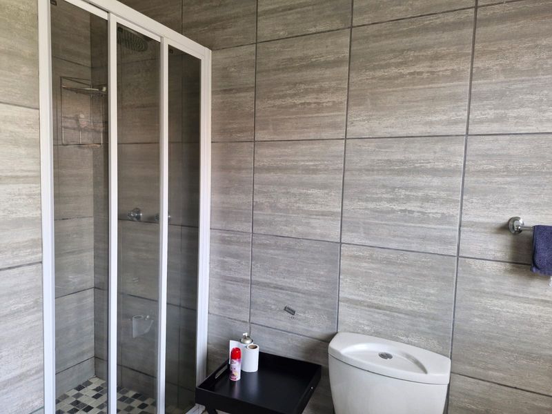 A modern bathroom featuring floor-to-ceiling grey textured wall tiles, a glass shower enclosure, and a standard toilet.