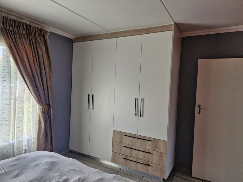 A well-maintained bedroom featuring modern built-in wardrobes with a combination of white and wood-grain finishes and tiled flooring.