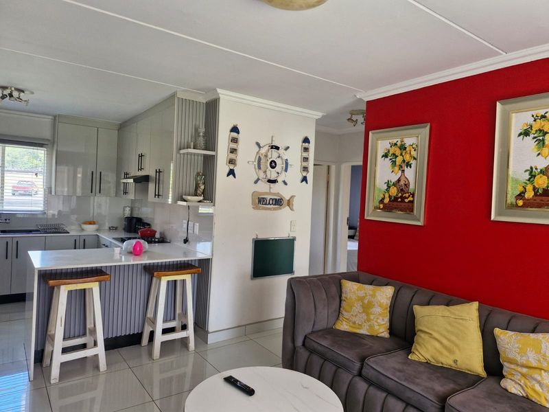 Open-plan living area featuring a modern kitchen with stone countertops, breakfast bar, and tiled flooring, seamlessly connected to the lounge space.