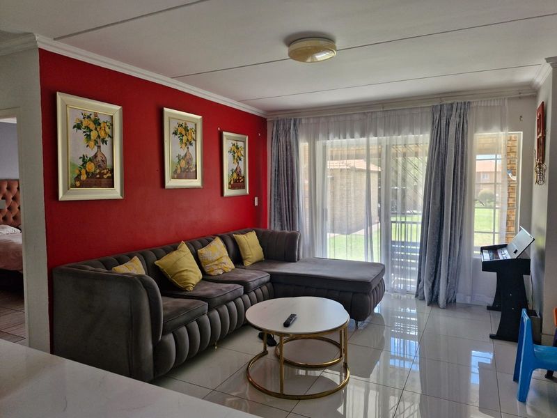 A bright living room featuring polished tiled flooring, a prominent red accent wall, and large sliding glass doors providing access to the outdoor area.