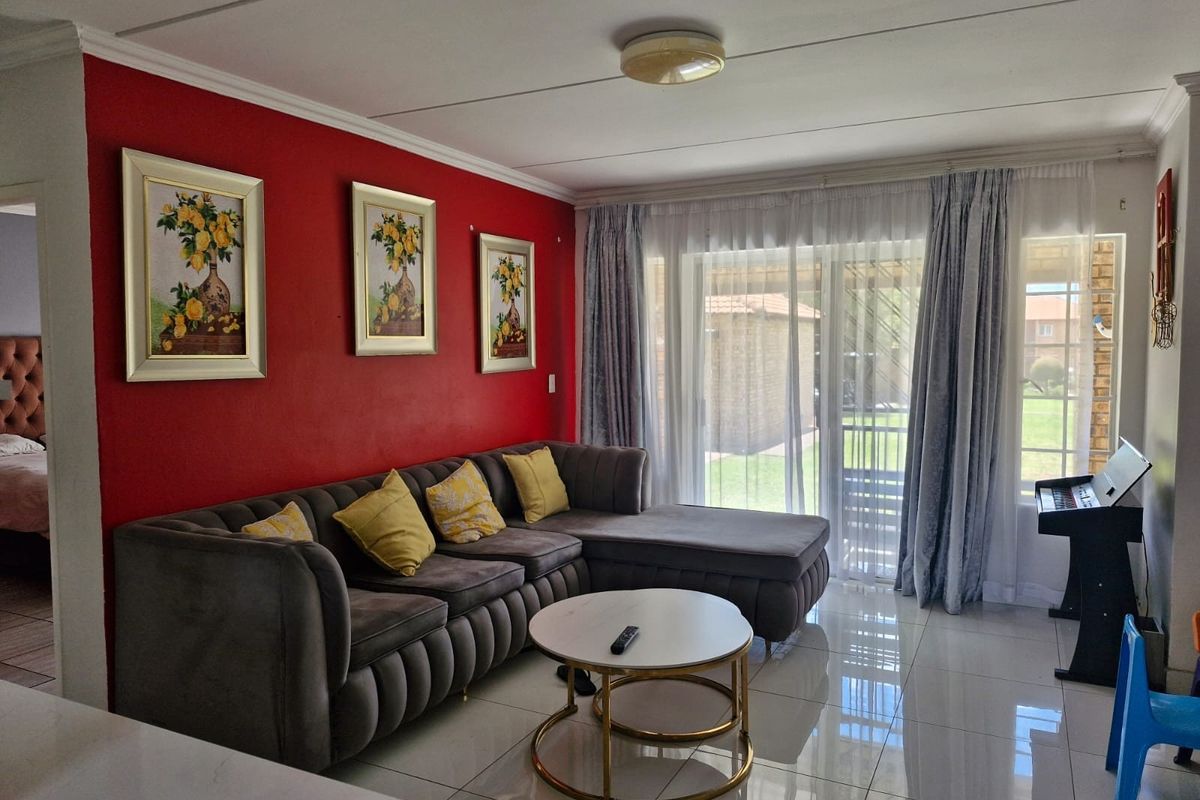 A bright living room featuring polished tiled flooring, a prominent red accent wall, and large sliding glass doors providing access to the outdoor area.