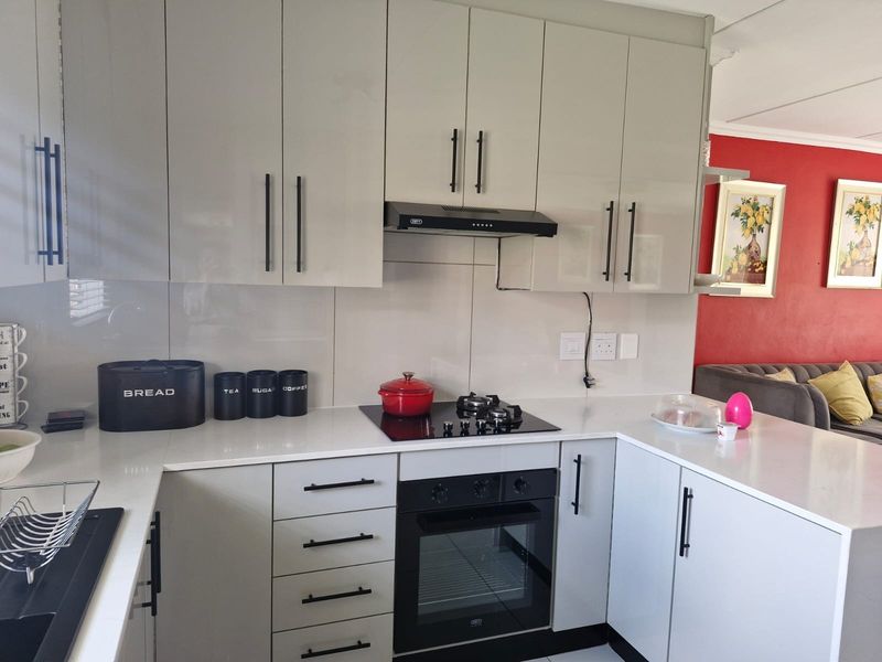 Modern kitchen featuring sleek light grey cabinetry, white quartz countertops, glass splashback, and integrated appliances including a gas hob and built-in oven.