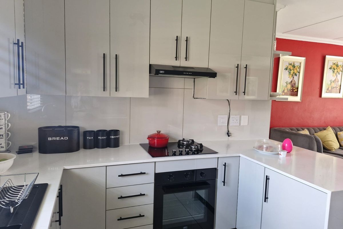 Modern kitchen featuring sleek light grey cabinetry, white quartz countertops, glass splashback, and integrated appliances including a gas hob and built-in oven.