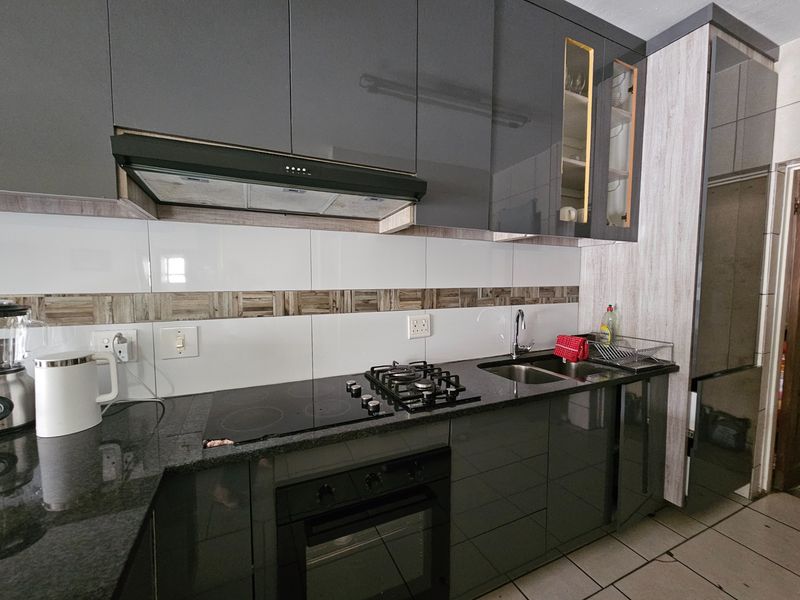Modern kitchen featuring high-gloss grey cabinetry, granite countertops, a dual gas and electric hob, built-in oven, and a sleek tiled backsplash.