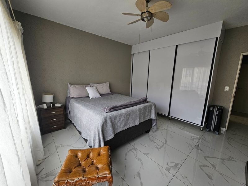 A well-maintained bedroom featuring modern marble-look tiled flooring, a large built-in wardrobe with sliding doors, and a ceiling fan.