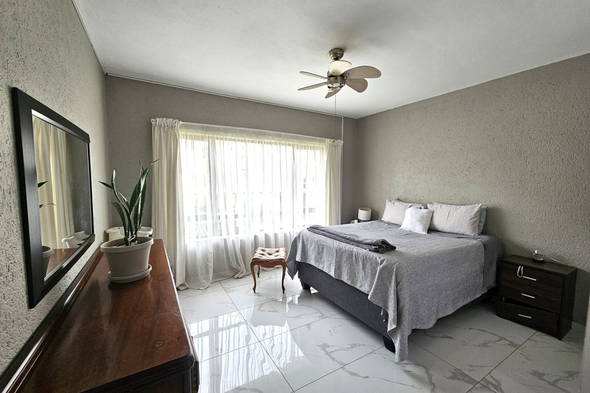 A well-lit bedroom featuring large windows, a ceiling fan, and modern marble-look tiled flooring.