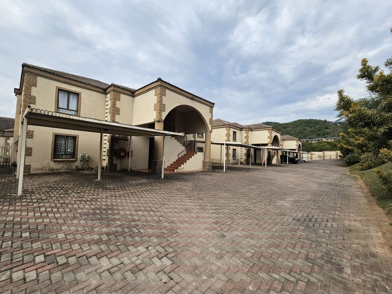 Exterior view of an apartment complex featuring paved driveway, covered parking carports, and stone-accented building facades.