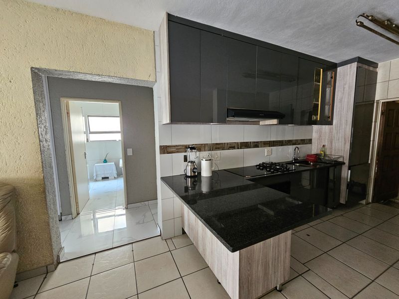 Modern kitchen featuring dark cabinetry, granite countertops, gas hob, and tiled flooring, with an adjacent doorway leading to a secondary room.