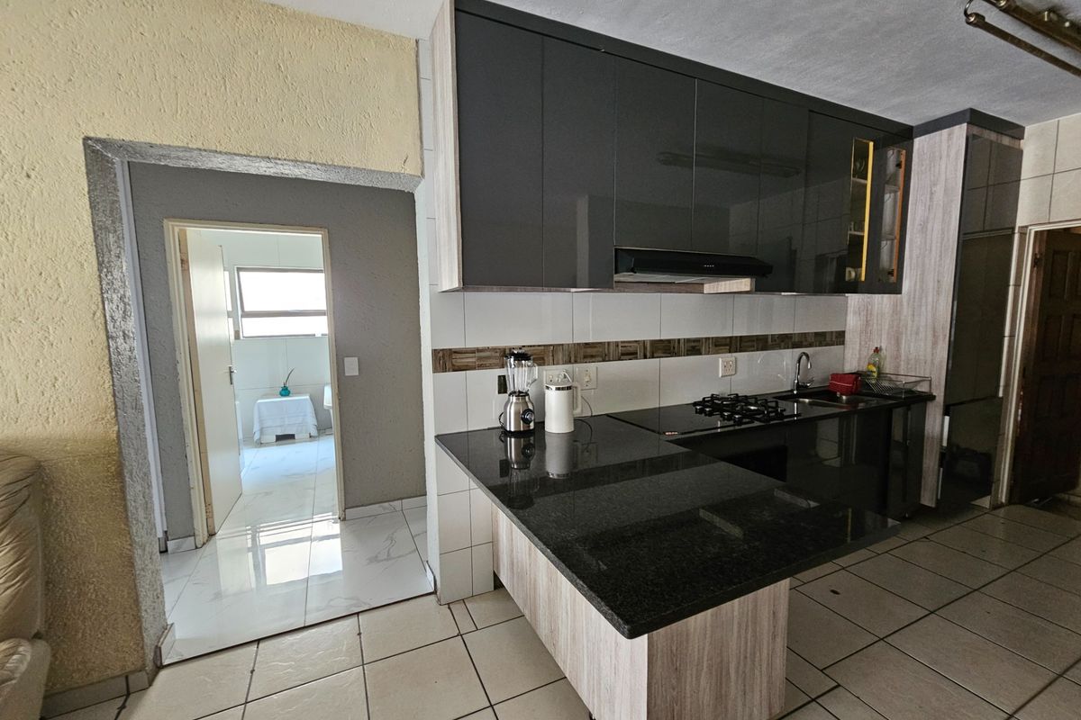 Modern kitchen featuring dark cabinetry, granite countertops, gas hob, and tiled flooring, with an adjacent doorway leading to a secondary room.