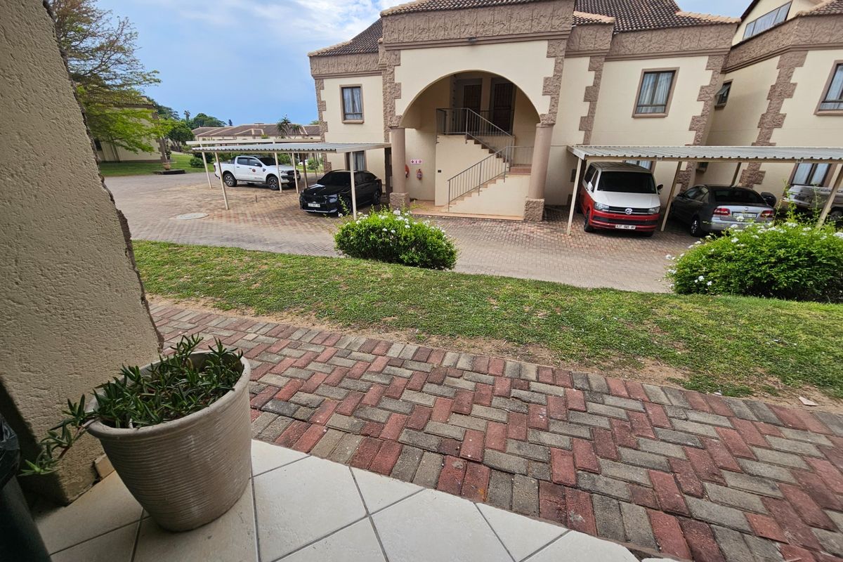 View of the apartment complex exterior featuring a paved patio area, covered carports, and a communal garden space.