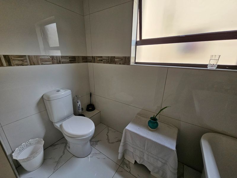 A clean, modern bathroom featuring white tiled walls with decorative accents, marble-look floor tiles, a standard toilet, and a bathtub.
