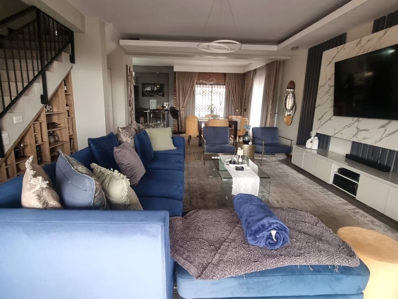 Spacious open-plan living area featuring a modern media wall, recessed ceiling lighting, and a staircase with a contemporary metal balustrade.
