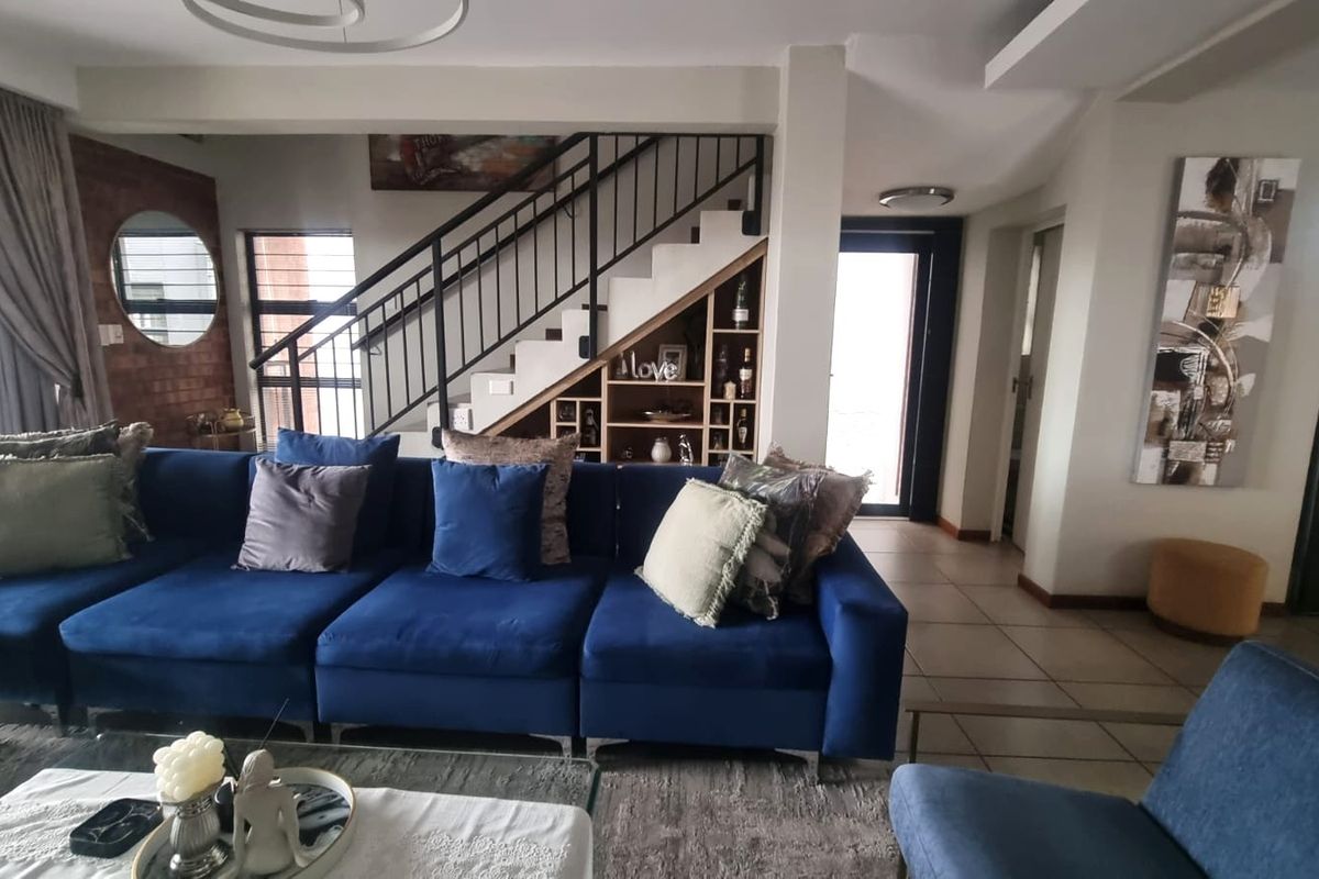 Spacious living room featuring a modern staircase with metal balustrade, built-in under-stair shelving, and an exposed brick feature wall.