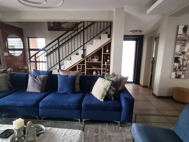 Spacious living room featuring a modern staircase with metal balustrade, built-in under-stair shelving, and an exposed brick feature wall.