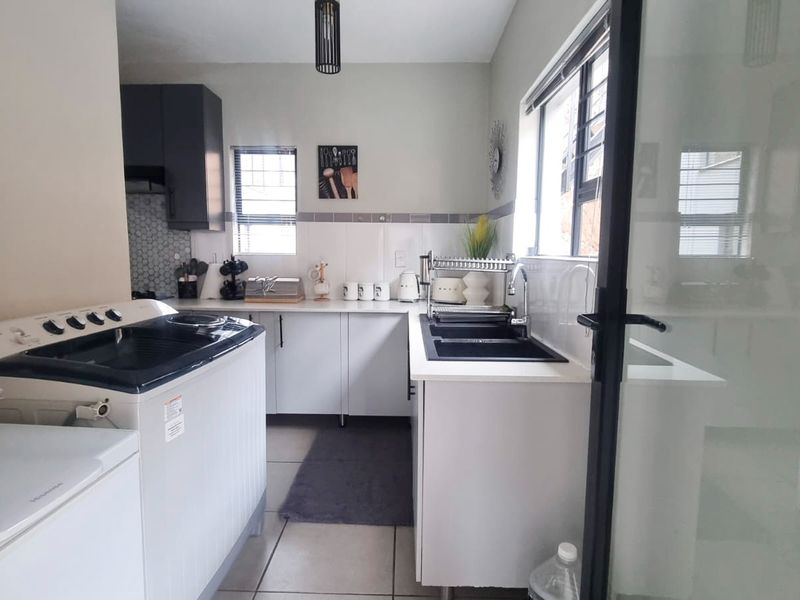 A functional scullery featuring built-in cabinetry, a double sink, tiled backsplash, and tiled flooring, providing additional prep and wash-up space.