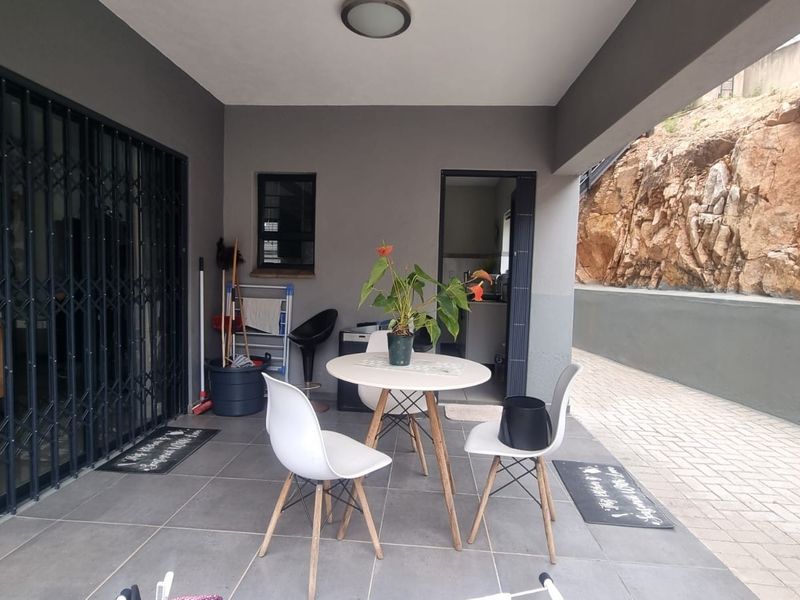 A covered patio area featuring tiled flooring, a security gate, and a view of the adjacent natural rock retaining wall.