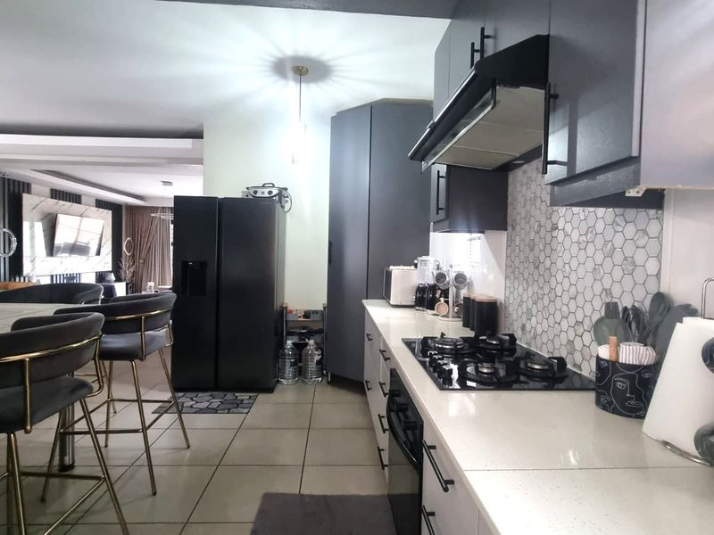 Modern open-plan kitchen featuring sleek dark cabinetry, quartz countertops, a gas hob with extractor, and a stylish hexagonal tile backsplash.