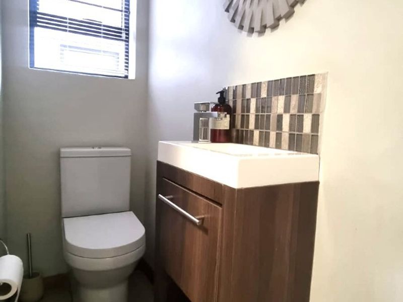 A compact, modern bathroom featuring a sleek vanity cabinet with a basin, mosaic tile splashback, and a toilet.