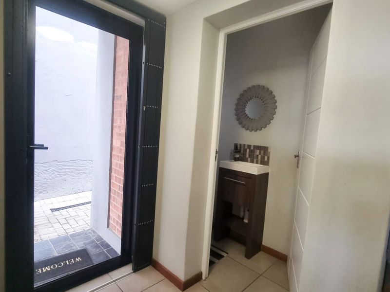 A functional hallway area featuring a glass door leading to an outdoor space and a compact guest bathroom with a modern vanity and basin.