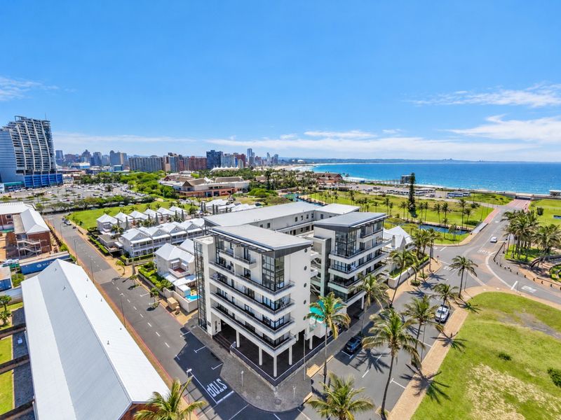 Aerial view of a modern apartment complex featuring balconies, a swimming pool, and proximity to the coastline and urban amenities.