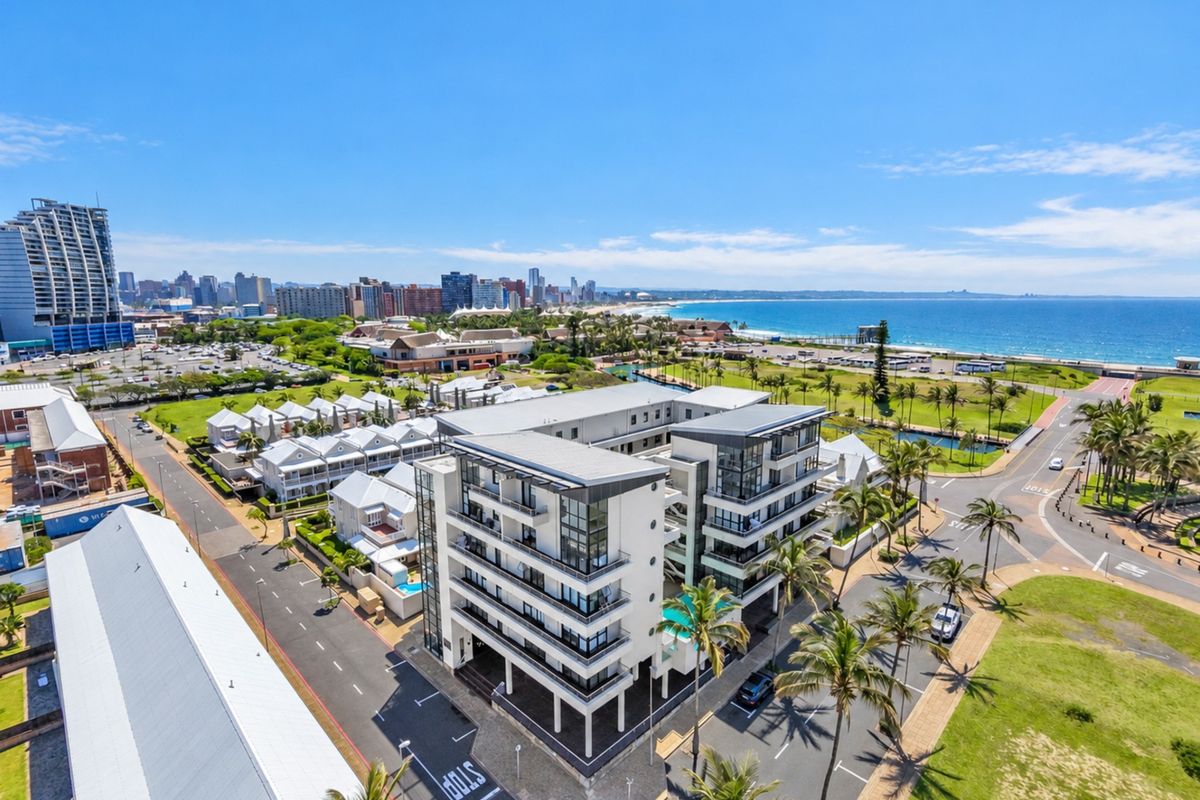 Aerial view of a modern apartment complex featuring balconies, a swimming pool, and proximity to the coastline and urban amenities.