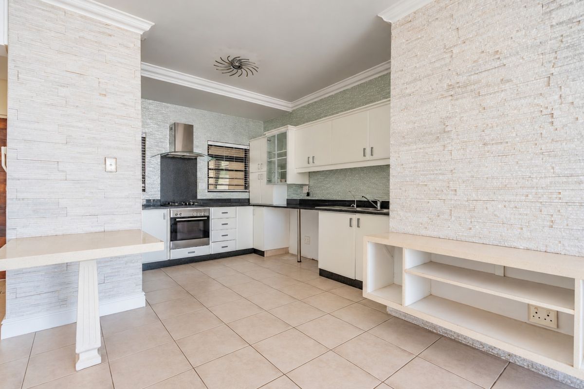 A spacious, empty kitchen featuring white cabinetry, stone-clad feature walls, built-in oven with extractor fan, and neutral ceramic floor tiles.