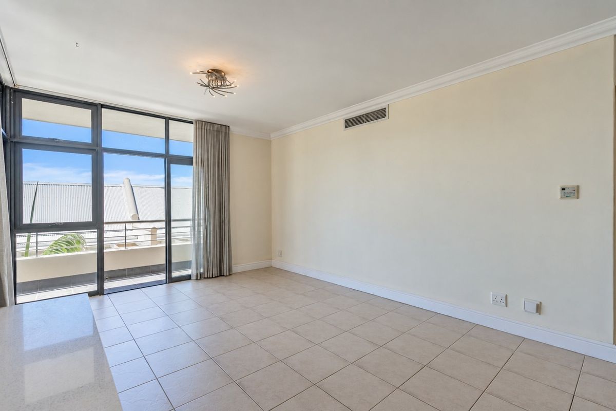A bright and spacious empty living area featuring tiled floors, ducted air conditioning, and large sliding glass doors leading to a private balcony.