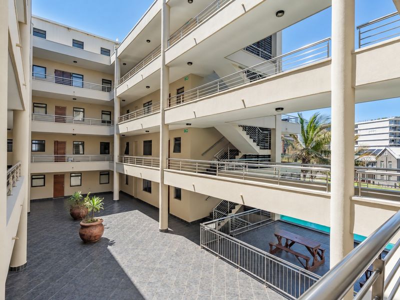 A multi-level apartment complex courtyard featuring tiled flooring, metal railings, and open-air walkways connecting the residential units.