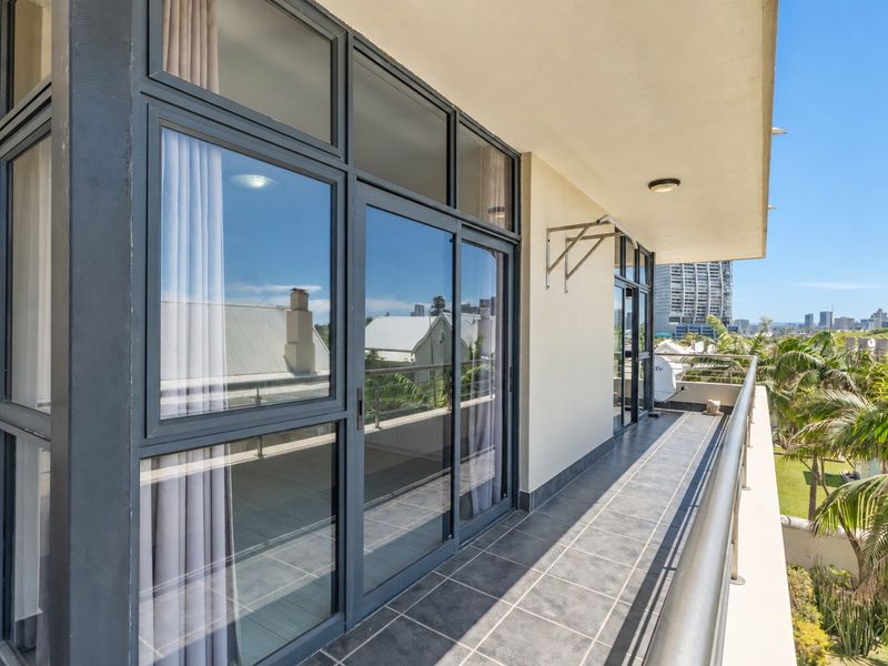 A spacious, modern balcony featuring tiled flooring, sleek sliding glass doors, and a metal railing, offering an elevated view of the surrounding area.